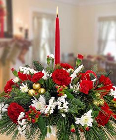 a christmas centerpiece with red and white flowers, greenery, candlesticks and other holiday decorations