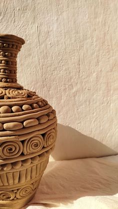 a brown vase sitting on top of a table next to a white wall and shadow