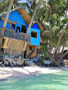 a blue house sitting on top of a sandy beach next to the ocean with palm trees