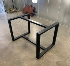 two black metal tables sitting on top of a cement floor in front of a wall