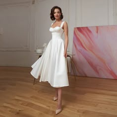 a woman in a white dress standing on a hard wood floor next to a painting