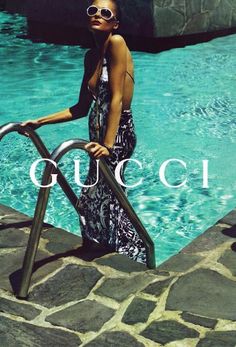 a woman leaning on a railing next to a swimming pool with the words gucci in front of her