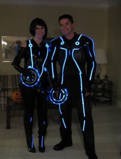 two people dressed in black and blue standing next to each other with neon lights on their body