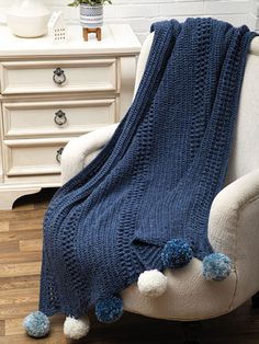 a white chair with a blue knitted blanket on it and pom - poms