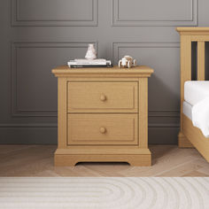 a small wooden nightstand next to a bed in a room with gray walls and hardwood floors