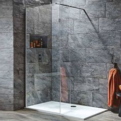 a walk in shower sitting next to a wall with gray tiles on it and a towel hanging from the side