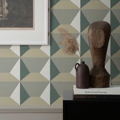 a vase sitting on top of a wooden table next to a wallpapered wall