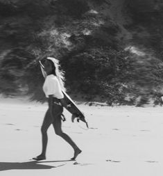 a woman walking across a sandy beach holding a surfboard