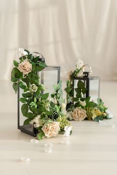 two glass vases with flowers and greenery on them