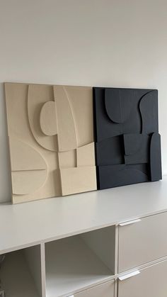 two abstract paintings on the wall next to each other in an empty room with white drawers