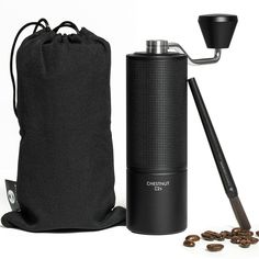 the coffee grinder is next to a black bag and some coffee beans are scattered around it