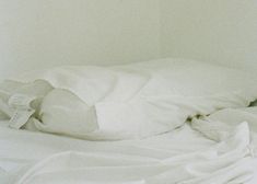 an unmade bed with white sheets and pillows