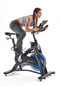 a woman is riding an exercise bike with a laptop on the handlebars and looking at her phone