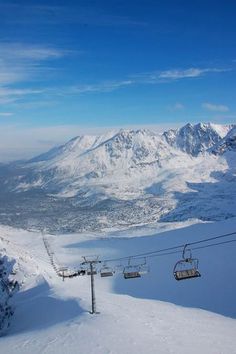 a ski lift going up the side of a snow covered mountain with mountains in the background