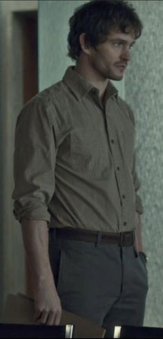 a man standing in front of a wall wearing a brown shirt