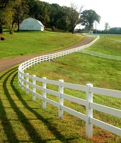 a white fence is in front of a grassy field with a barn on the other side