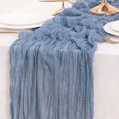 the table is set with white plates and silverware on it, along with a blue runner