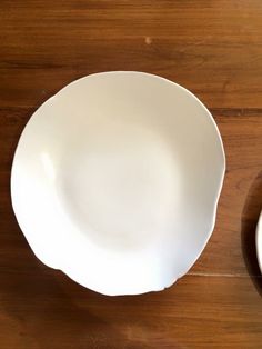 an empty white bowl next to a plate on a wooden table