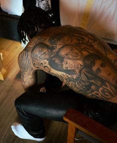 a man with tattoos on his back sitting in front of a table and looking down at the floor