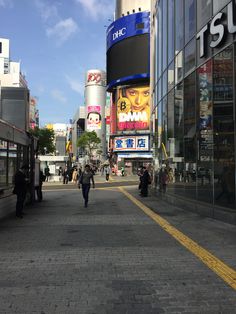 people are walking down the street in front of some tall buildings and billboards with chinese characters on them