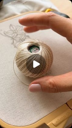 someone is holding yarn on top of a piece of fabric and pointing at the ball