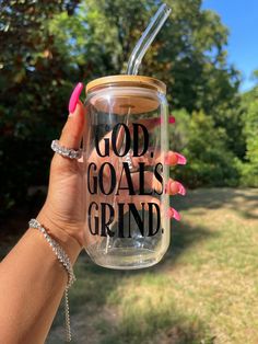 a person holding up a mason jar with the words god goats grind on it in front of some trees