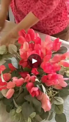 a woman is making a flower arrangement with red flowers