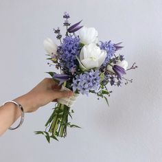 a hand holding a bouquet of white and purple flowers with greenery on the stems