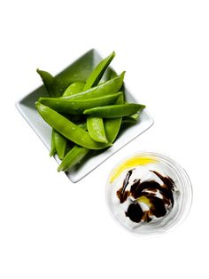 some green beans are on a white plate next to a small bowl of oil and sauce