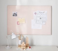 a white desk topped with a lamp next to a pink bulletin board