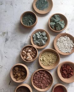 seven bowls filled with different colored powders on top of a white countertop next to each other