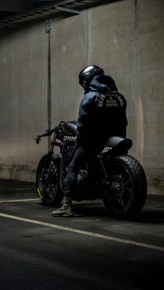 a man riding on the back of a motorcycle in a parking lot next to a wall