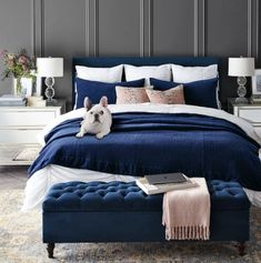 a blue bed with white sheets and pillows in a gray room next to two nightstands