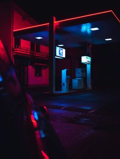 an empty gas station at night with red and blue lights on the side of the building