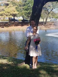 a man and woman standing next to each other near a tree in front of a lake