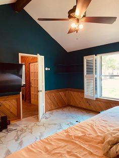 an empty bedroom with blue walls and wood paneling on the wall, ceiling fan and flat screen tv