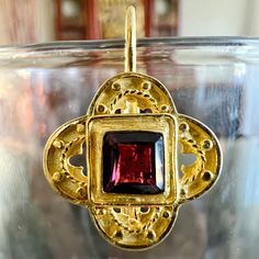 a gold pendant with a red stone in the center on a clear glass bowl,