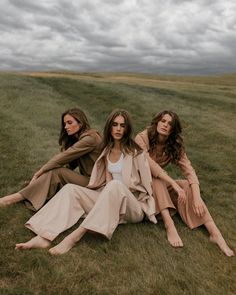 three women sitting in the grass on a cloudy day