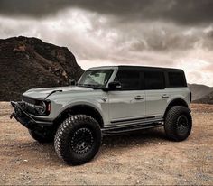 a white truck parked on top of a dirt field next to a large rock formation