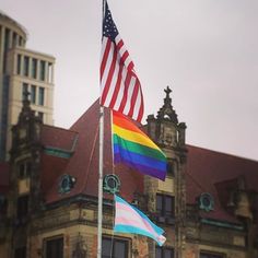 an american and rainbow flag flying in front of a building