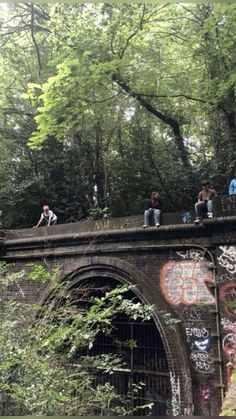 people sitting on the edge of a bridge covered in graffiti