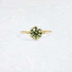 a green diamond ring sitting on top of a white surface with the center stone in yellow gold