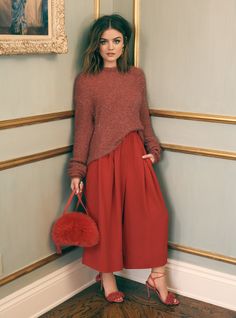 a woman standing in front of a wall holding a red purse and posing for the camera