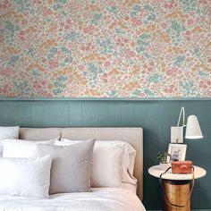 a bedroom with floral wallpaper and white linens on the bed, along with an end table