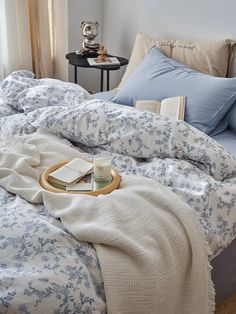 an unmade bed with blue and white comforter on it, next to a night stand