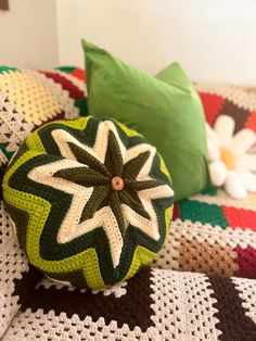 a green and white crocheted pillow sitting on top of a bed next to pillows