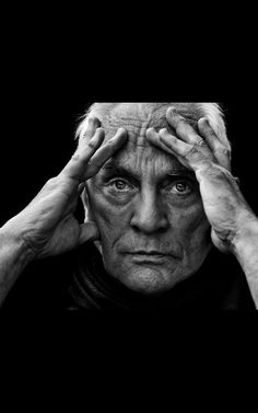 an old man holding his hands to his head and looking at the camera, black and white photo