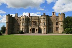 a large castle like building sitting in the middle of a lush green field under a blue cloudy sky