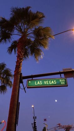 a street sign hanging from the side of a pole next to a palm tree at night