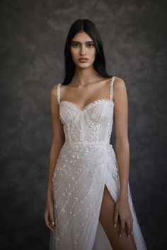 a woman with long black hair wearing a white dress and standing in front of a dark background